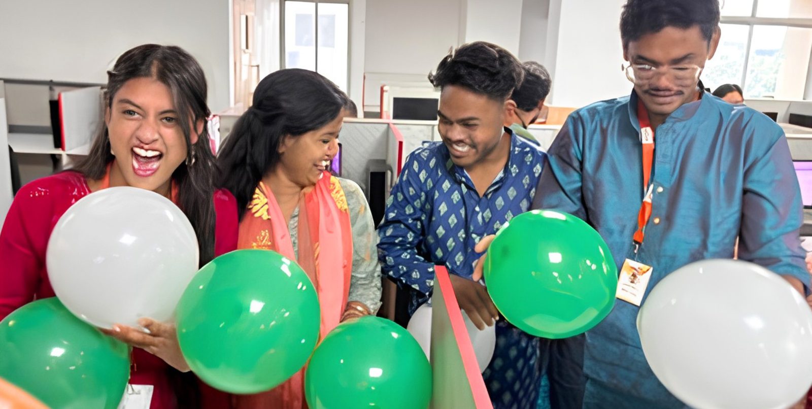 Teammates laughing with green and white balloons at an office celebration